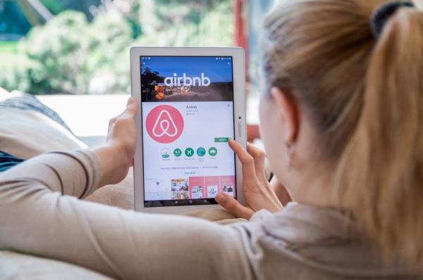 A woman looking at a phone with the Airbnb app open.