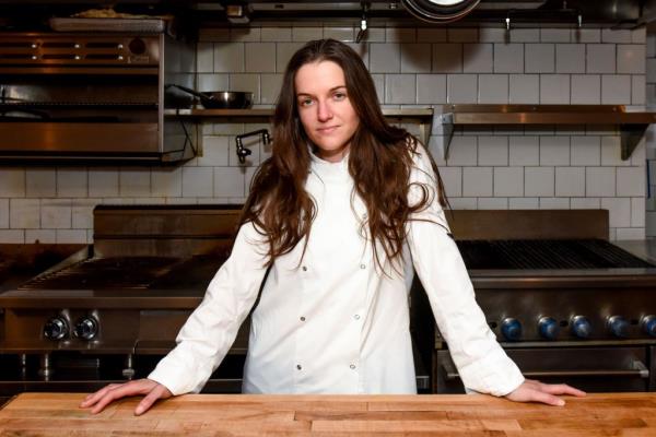 Liz Johnson in chef whites, standing in front of a counter in a restaurant kitchen. 