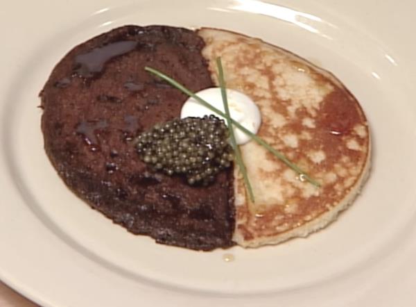 Caviar in top of a circular blini which is rye on one side and white flour on the other, garnished with a spring o<em></em>nion stalk