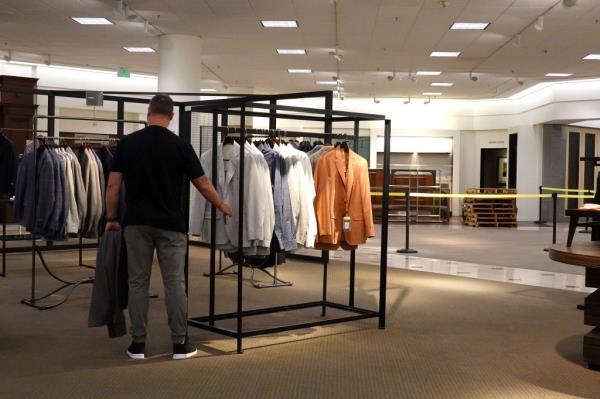 A man is seen perusing rack of clothes next to a roped-off section of the store