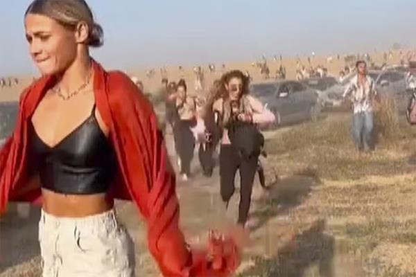 A woman with a pained look in red and a black crop top runs in the desert while others run behind her
