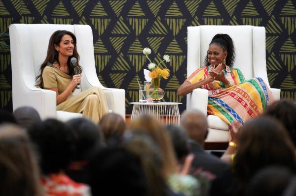 Michelle Obama smiling and clapping while Amal Cloo<em></em>ney speaks into a microphone