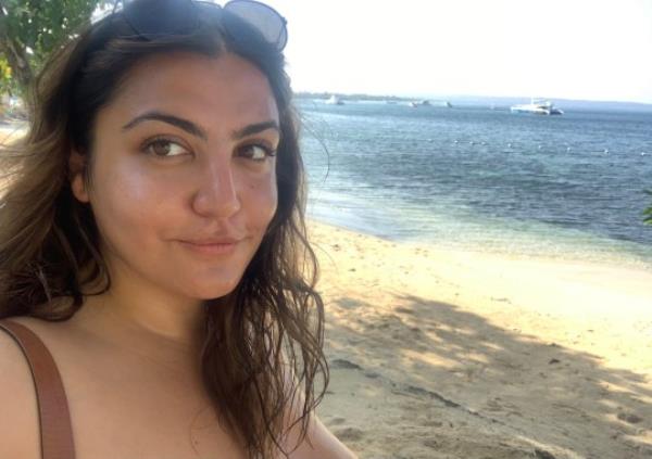 Almara at a beach with sunglasses on her head, looking to camera and smiling