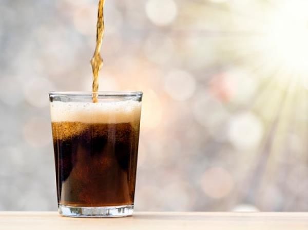 Glass of drink with cola illuminated by sunlight.