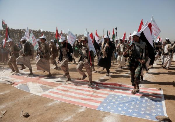 Houthi fighters walking over British and US flags at a rally in Sana'a, Yemen, in support of Palestinians and recent attacks on shipping.