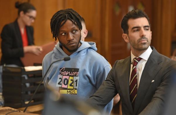 Jordan Williams in a blue sweatshirt at his arraignment at Brooklyn Criminal Court, standing next to another suited individual.