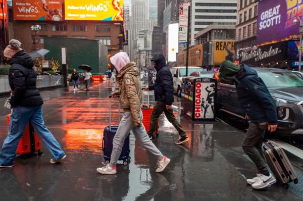 Tourists with their rolling suitcases schlep through rain and sleet in Times Square in New York.