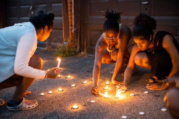 Sandriana McBroom, right, and Makhiya Mcbroom, center, light candles that spell out 