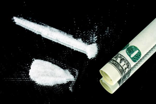 A close up of cocaine lines on a mirror with a rolled banknote, reflecting substance abuse and addiction, in a dark studio lighting setting.