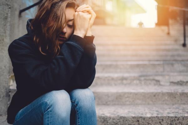 Depressed teenage girl sitting thoughtfully on stairs, with her hands covering her face