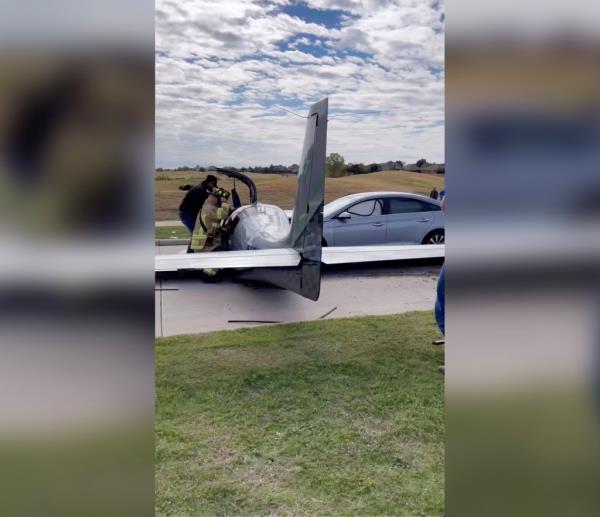A paramedic and a firefighter tend to the passengers of a small silver airplane that had just crashed into a silver sedan on a roadway.