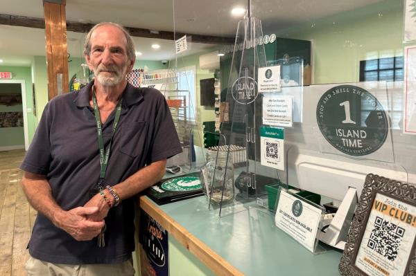 Geoff Rose, owner of Island Time cannabis dispensary, standing in his store in Vineyard Haven, Mass, posing next to a counter amid a potential pot shortage
