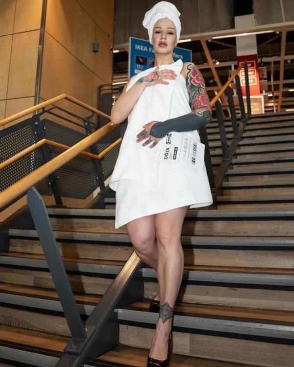 A woman modeling a towel dress and stilettos in an Ikea store, recreating Doja Cat's Met Gala outfit.