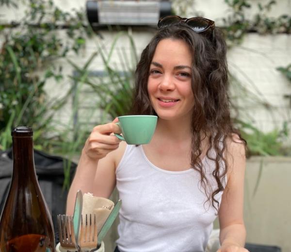 Haley looks relaxed, holding a cup of tea, she is wearing a white vest