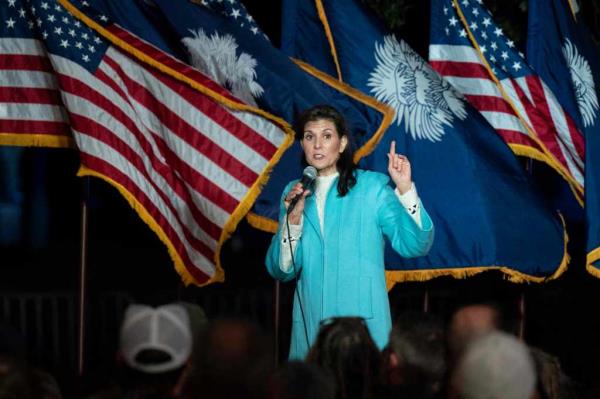 Nikki Haley speaking into a microphone with flags behind her.