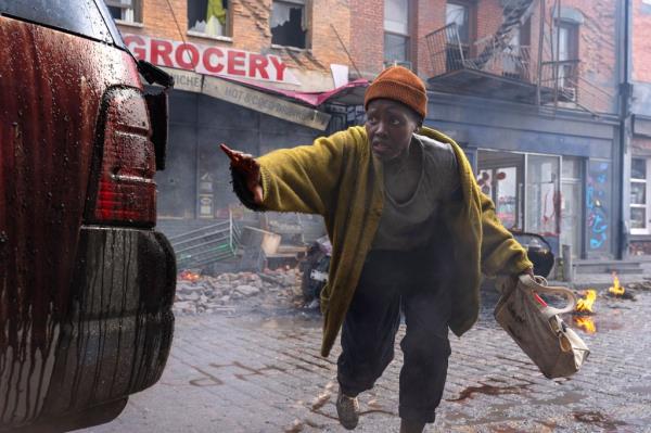 Lupita Nyong'o crouches behind an SUV in a scene from 