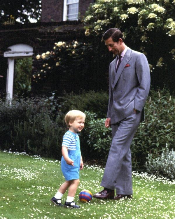 Prince Charles in a suit standing next to a young Prince William playing with a ball