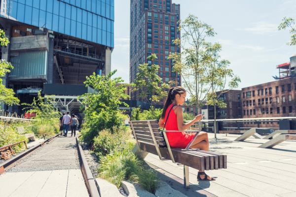 Woman sitting alone on a bench in New York City's High Line park, using her smartphone in the morning before crowds appear