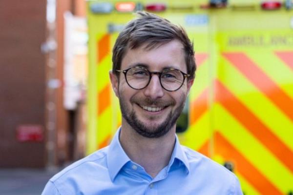 Jo<em></em>nathan Iliff in portrait in front of ambulance. He is smiling, and wearing glasses
