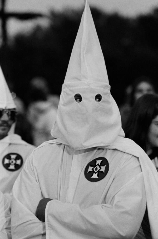 A person wearing a white hooded robe, identified as a member of the Ku Klux Klan