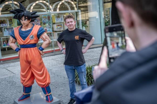 A fan takes a picture next to a statue of Dragon Ball character 