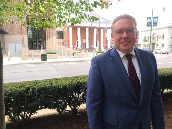 Secretary of the Commo<em></em>nwealth Al Schmidt in a suit and tie standing outdoors in Chambersburg, with Franklin County's Old Courthouse and Judicial Center in the background.