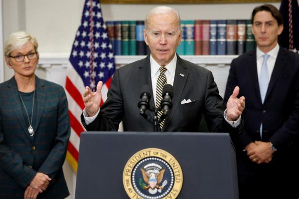 President Joe Biden delivers remarks at the White House podium with Energy Secretary Jennifer Granholm and Amos Hochstein beside him.