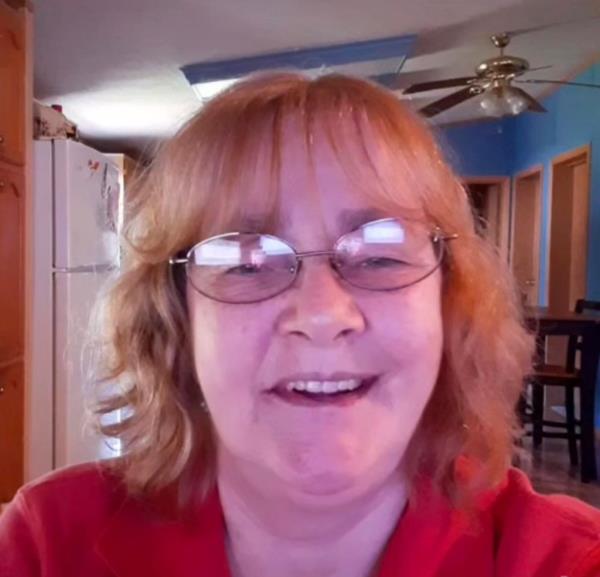 Florence Harrelson, a white woman with red hair wearing wire-rimmed glasses and a red top, smiles at the camera.