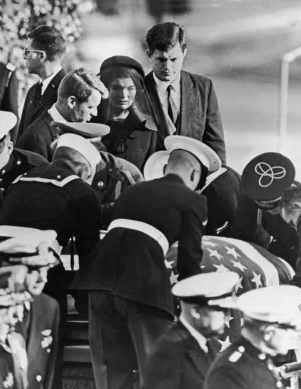 First Lady Jacqueline Kennedy stands between her brothers-in-law, Robert and Edward Kennedy, at the graveside of her husband, assassinated President John F. Kennedy, during his funeral.
