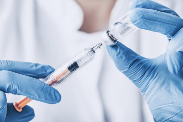 Two gloved hands withdrawal medication from a vial using a syringe.