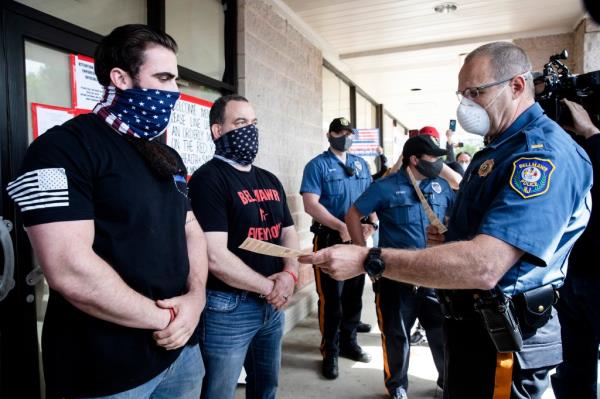 A police officer issues Atilis Gym co-owners Ian Smith, left, and Frank Trumbetti, center, summons outside their gym in Bellmawr, N.J., in May 2020.