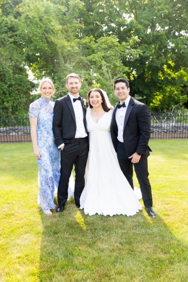Bride and groom in wedding clothes, standing between another man and woman, outdoors