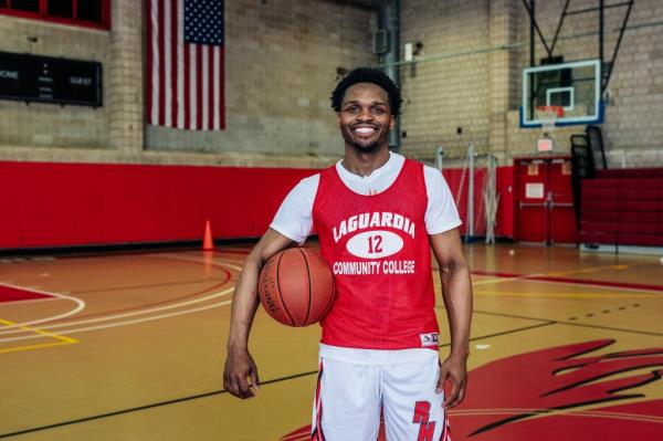 Arthur Dukes in practice jersey holds a basketball on a basketball court.