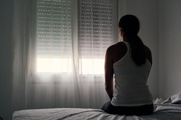 Rear view of an unrecognizable abused woman sitting on her bed looking out the window.