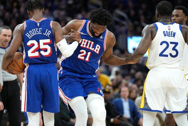 Joel Embiid #21 of the Philadelphia 76ers is helped up by Danuel House Jr. #25 and Draymond Green #23 of Golden State Warriors during a basketball game.