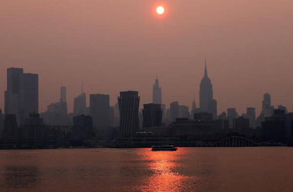 A New York Waterway ferry crossing the Hudson River at sunrise, with the Manhattan skyline obscured by haze and smoke from Canadian wildfires.
