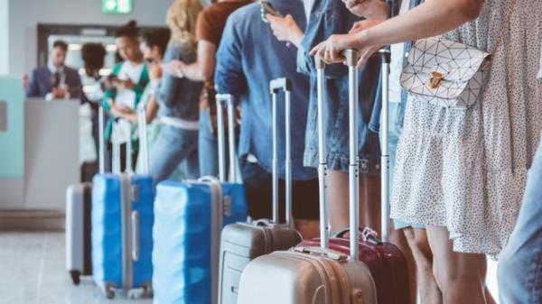 Travelers with luggage using smart pho<em></em>nes while waiting in line for boarding at airport. Focus on wheeled luggage.