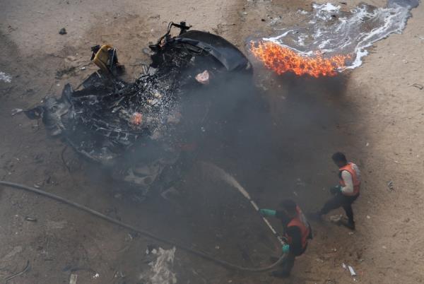 Two Palestinian men spray water on a burning car hit by an Israeli strike.