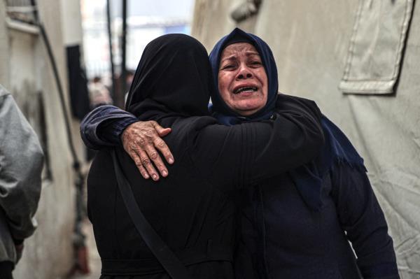 Two women wearing black clothing and head coverings embrace in tears amid the bombardment in southern Gaza.