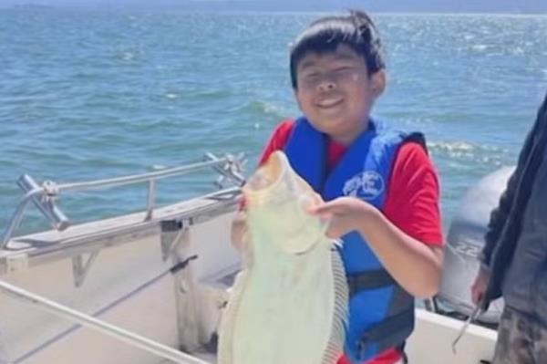 Juladi “Jude” Khammoungkhoune holds up a fish on a boat.