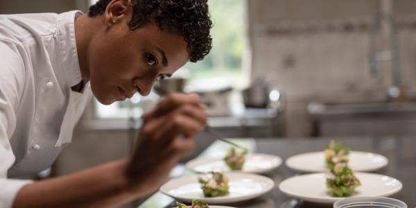 Ariana Debose leans over a plate while arranging food on it in House of Spoils